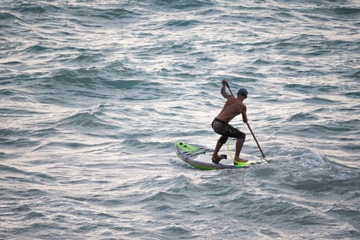 athletic wiry surfer guy swims with a paddle on a sup board in the sea Stand up paddleboarding