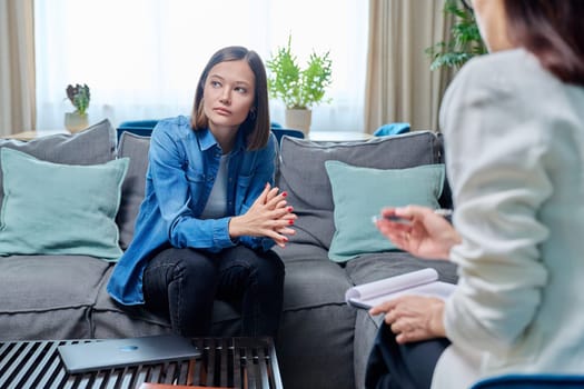 Sad young woman at therapy session with psychologist, psychiatrist. Therapist counselor and unhappy female patient on sofa in office. Psychology counseling treatment psychotherapy mental health youth