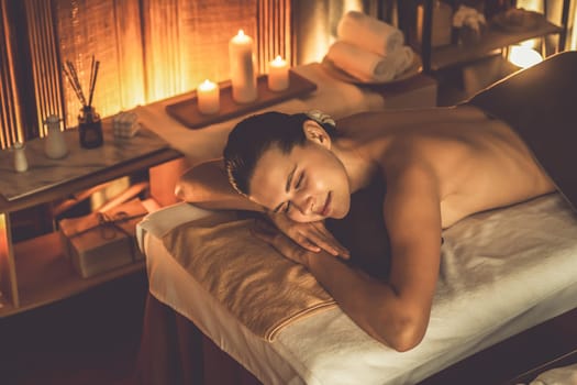 Caucasian woman customer enjoying relaxing anti-stress spa massage and pampering with beauty skin recreation leisure in warm candle lighting ambient salon spa at luxury resort or hotel. Quiescent