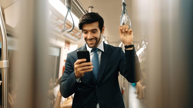 Professional smart business man looking phone while standing at train surrounded by people. Caucasian project manager checking email, planing marketing strategy with blurred background. Exultant.