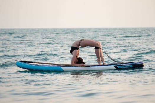 sporty girl on a sup board with a paddle in the sea does yoga