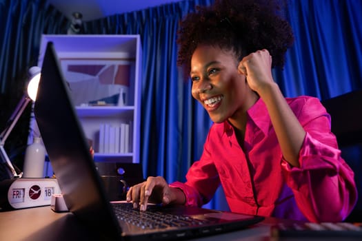 African woman blogger wearing pink shirt with happy face, looking on screen laptop with valued achievement project or get scholarship. Concept of cheerful expression work from home. Tastemaker.