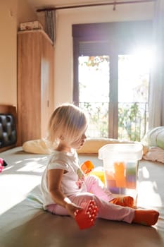 Little girl with a Lego constructor is sitting on the bed. Side view. High quality photo