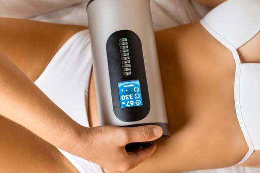 Beauty salon expert massages abdominal area with professional fat burning device. Procedure for healthy appearance of body part