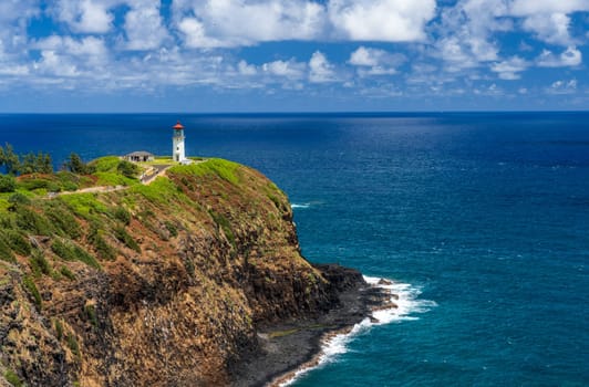 Kilauae Lighthouse on headland above turquoise ocean bay on the north coast of Kauai in Hawaii.