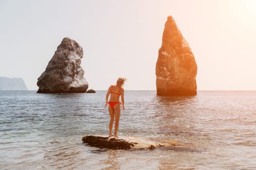 Woman travel sea. Young Happy woman in a long red dress posing on a beach near the sea on background of volcanic rocks, like in Iceland, sharing travel adventure journey