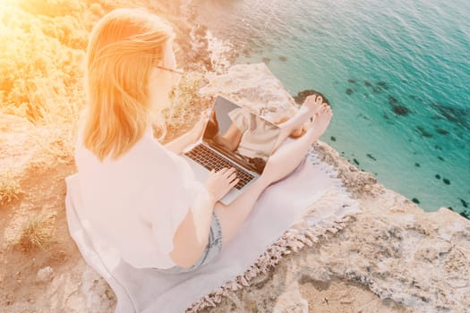 Woman sea laptop. Business woman in yellow hat working on laptop by sea. Close up on hands of pretty lady typing on computer outdoors summer day. Freelance, digital nomad, travel and holidays concept.