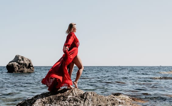 Woman travel sea. Young Happy woman in a long red dress posing on a beach near the sea on background of volcanic rocks, like in Iceland, sharing travel adventure journey