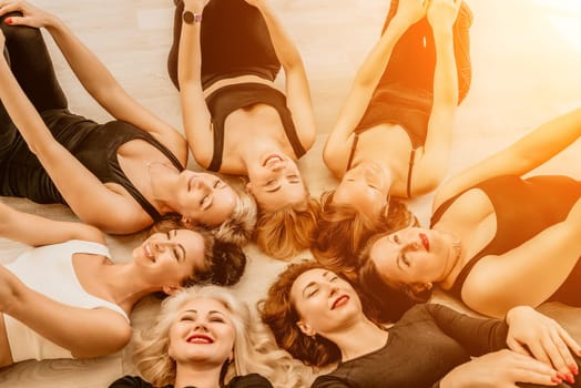 Group of young womans fitness instructor in Sportswear Leggings and Tops, stretching in the gym before pilates, on a yoga mat near the large window on a sunny day, female fitness yoga routine concept.