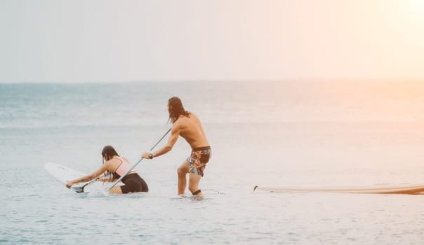 Sea woman and man on sup. Silhouette of happy young woman and man, surfing on SUP board, confident paddling through water surface. Idyllic sunset. Active lifestyle at sea or river