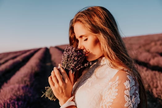 Close up portrait of young beautiful woman in a white dress and a hat is walking in the lavender field and smelling lavender bouquet.