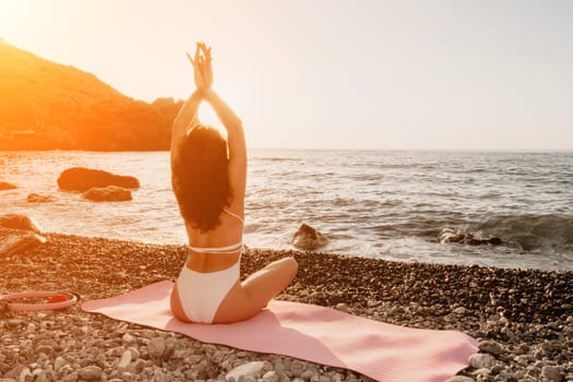 Young woman in swimsuit with long hair practicing stretching outdoors on yoga mat by the sea on a sunny day. Women's yoga fitness pilates routine. Healthy lifestyle, harmony and meditation concept.