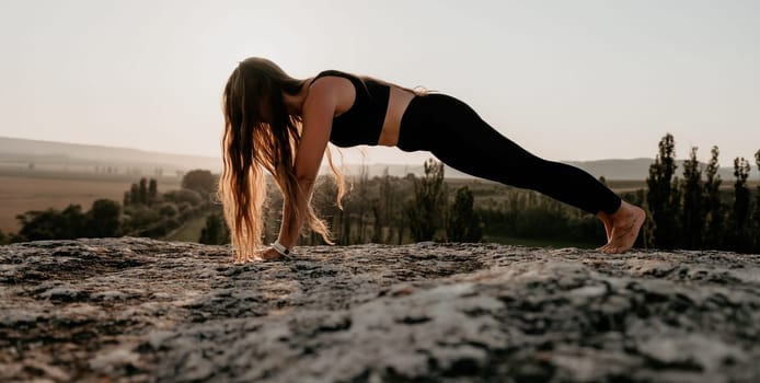 Well looking middle aged woman with long hair, fitness instructor in leggings and tops doing stretching and pilates on the rock near forest. Female fitness yoga routine concept. Healthy lifestyle.