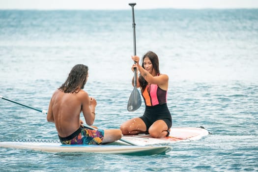 Sea woman and man on sup. Silhouette of happy young woman and man, surfing on SUP board, confident paddling through water surface. Idyllic sunset. Active lifestyle at sea or river