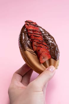 Human Hand Holds Genital Vagina, Vulva Shaped Waffle With Strawberries, Dark Chocolate On Pink Background. Festival Street Food, Sweet Cookie Vertical Plane.