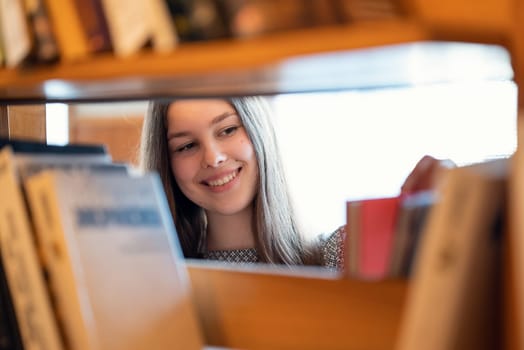 Portrait of a girl between shelves in university library looking for literature