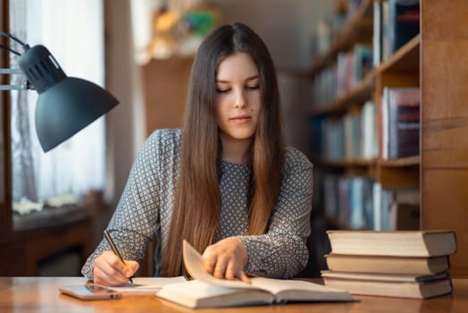 Student girl studying for exams in university library, working at the desk