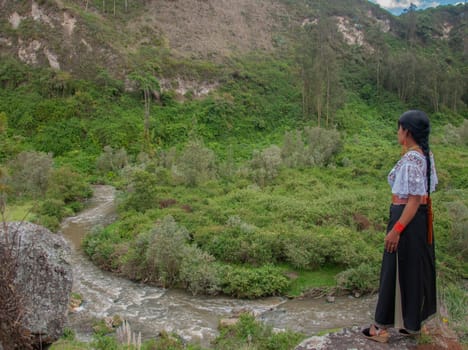 indigenous woman in traditional dress at the edge of a canyon looking at the jungle landscape and a river flowing beneath her feet. earth day. High quality photo
