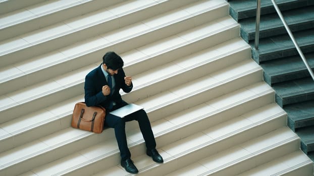 Top view business man celebrate successful project while sitting at stairs. Smart project manager getting new gob, getting promotion, increasing sales while calling friends by using laptop. Exultant.