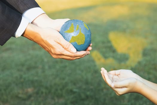 Businessman hand giving Earth globe to little boy as Earth day concept as corporate social responsible to contribute greener environmental protection for sustainable future generation. Gyre