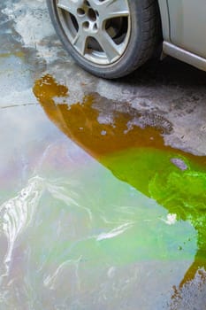 puddle of green coolant and brown technical liquids on the concrete floor near car.