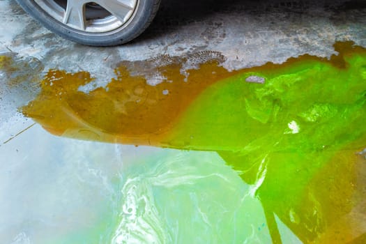 puddle of green coolant and brown technical liquids on the concrete floor near car.