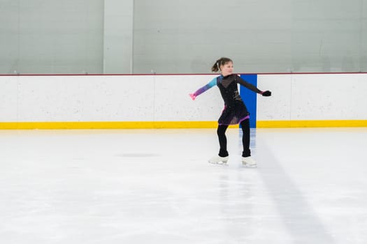 Young girl perfecting her figure skating routine while wearing her competition dress at an indoor ice rink.