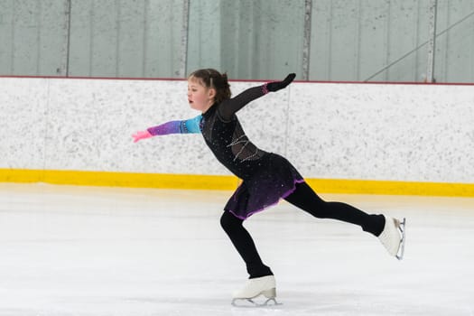 Young girl perfecting her figure skating routine while wearing her competition dress at an indoor ice rink.