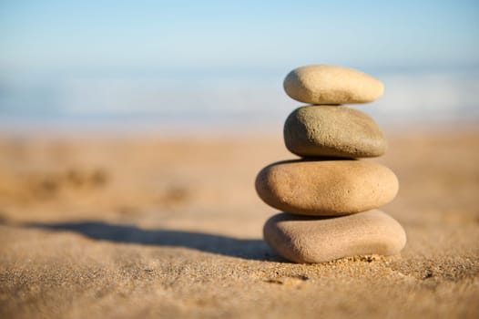 Still life. A pyramid of balanced stones stacked on sand against sea background. Stacked pebbles. The concept of balance and harmony. Sandy beach, calm sea, travel destination. Copy advertising space