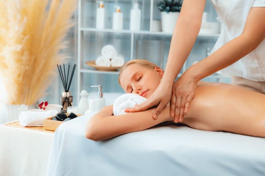 Caucasian woman customer enjoying relaxing anti-stress spa massage and pampering with beauty skin recreation leisure in day light ambient salon spa at luxury resort or hotel. Quiescent