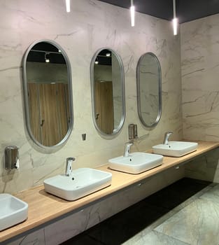 Modern restroom interior with stone gray tiles. Contemporary interior of public toilet. minimal interior with white tiles, round mirrors. Perspective of men's restroom. commercial bathroom.