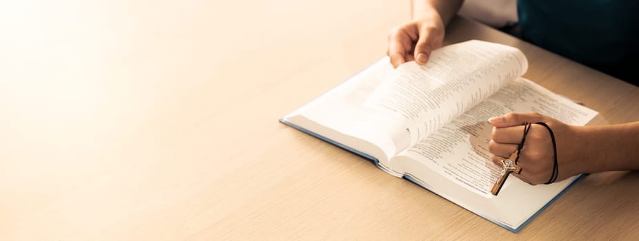 Cropped image of female reading a bible book while holding cross at wooden table with blurring background. Concept of hope, religion, faith, christianity and god blessing. Warm. Burgeoning.