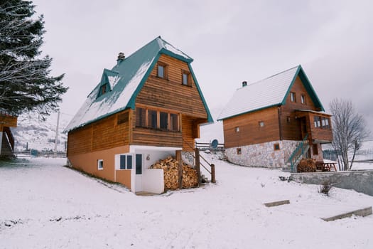 Wooden two-story cottages with woodpiles under the stairs in a snowy village. High quality photo