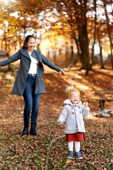 Smiling mom throws up fallen leaves over a little laughing girl in an autumn park. High quality photo
