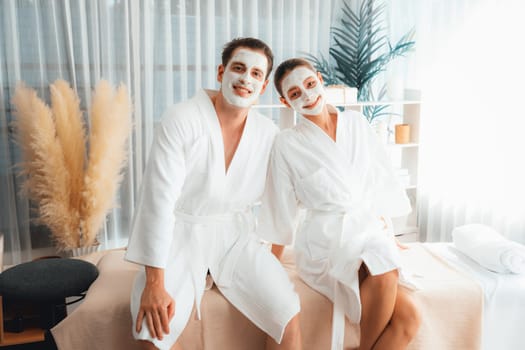 Blissful couple in bathrobe with facial cream mask enjoying serene ambiance of spa salon resort or hotel during holiday. Pampering face spa and skincare treatment with essence relaxation. Quiescent