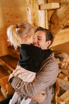 Smiling dad hugs little girl standing on his lap and hugging his neck. High quality photo