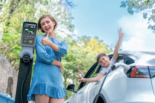 Family road trip vacation with electric vehicle, mother and son recharge EV car with green and clean energy. Nature and travel with eco-friendly car for sustainable environment. Perpetual