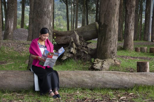 young indigenous girl sitting on a large tree trunk relaxing while reading a map from behind felled trees. earth day. High quality photo