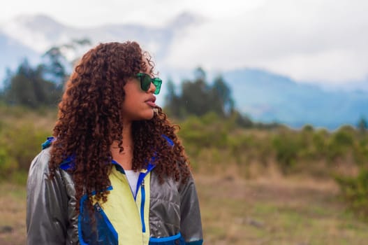 attractive young latin guy from ecuador with curly hair and mountain jacket looking at the copyspace and mountain background. earth day. High quality photo