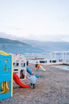 Little girl goes to the slide on the beach near the sea. Back view. High quality photo