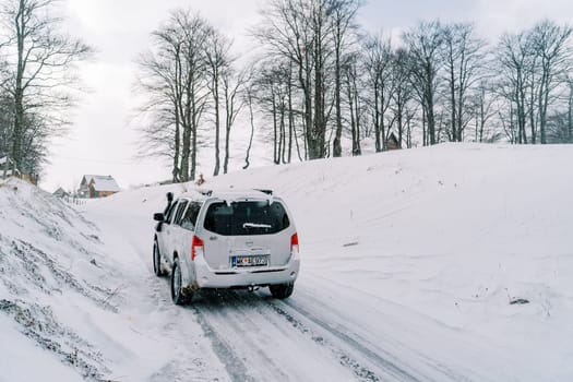 SUV drives along a snowy road in a village. Back view. High quality photo