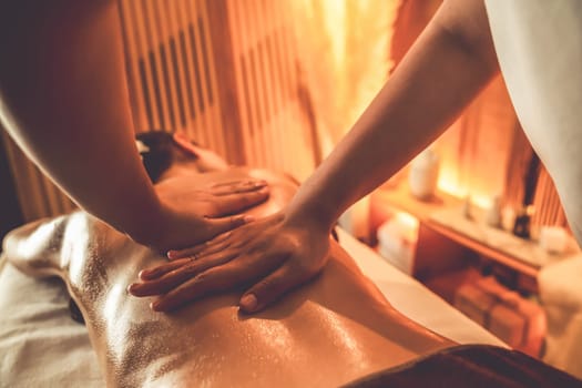 Closeup woman customer enjoying relaxing anti-stress spa massage and pampering with beauty skin recreation leisure in warm candle lighting ambient salon spa at luxury resort or hotel. Quiescent