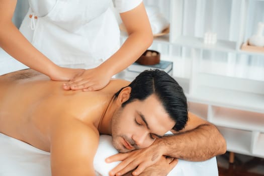 Caucasian man customer enjoying relaxing anti-stress spa massage and pampering with beauty skin recreation leisure in day light ambient salon spa at luxury resort or hotel. Quiescent