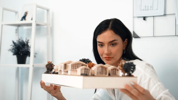 Close up of skilled young beautiful caucasian architect lift house model to check and focus on inspecting mistake point at modern office with blueprint. Creative design and living concept. Immaculate.