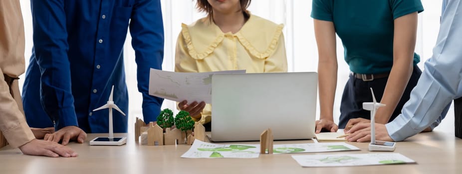 Professional business team prepare to present green business on table with windmill presented using renewable energy, wooden block and environmental document scatter around. Closeup. Delineation.