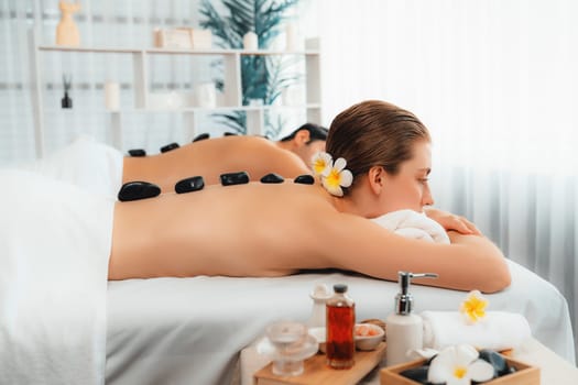 Hot stone massage at spa salon in luxury resort with day light serenity ambient, blissful couple customer enjoying spa basalt stone massage glide over body with soothing warmth. Quiescent