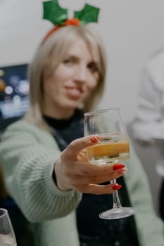 Portrait of one blurred blonde girl with a Christmas headband on her head and an outstretched hand and a glass of champagne, close-up side view with selective focus.