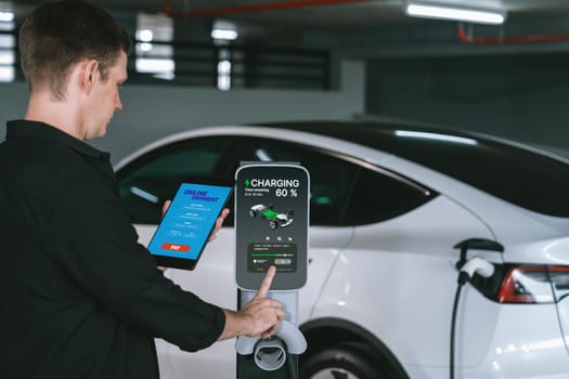 Young man travel with EV electric car to shopping center parking lot charging in downtown city showing urban sustainability lifestyle by green clean rechargeable energy of electric vehicle innards