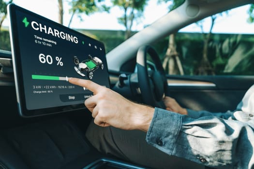 Electric car driver checks battery charging status, range and charging limit on app screen in the car. Smart technology device show EV car recharging data of electric storage in car battery innards.