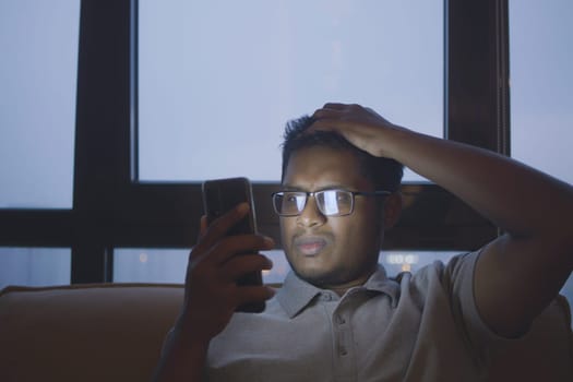 men s sitting on sofa using smart phone at night .